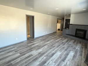 Unfurnished living room featuring a baseboard radiator, a fireplace, baseboards, and wood finished floors