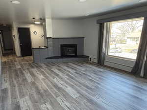 Unfurnished living room with a fireplace, baseboard heating, and wood finished floors