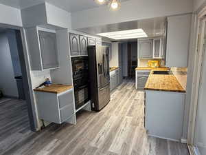 Kitchen with gray cabinets, butcher block counters, stainless steel fridge, and black oven