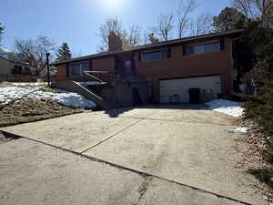 View of front of house featuring brick siding, driveway, a chimney, and an attached garage