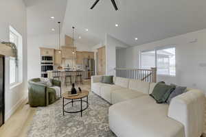 Living room with ceiling fan, high vaulted ceiling, sink, and light wood-type flooring