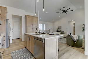 Kitchen with light brown cabinetry, decorative light fixtures, sink, stainless steel appliances, and a center island with sink