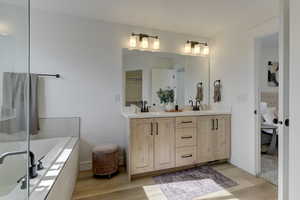 Primary Bathroom featuring vanity, tiled tub, and wood-type flooring