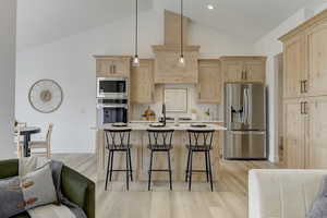 Kitchen featuring decorative light fixtures, a breakfast bar area, light brown cabinets, and appliances with stainless steel finishes