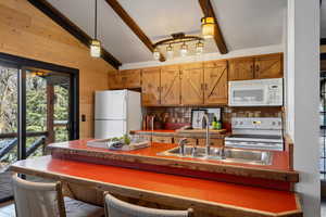 Kitchen with sink, hanging light fixtures, vaulted ceiling with beams, wood walls, and white appliances