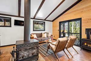 Living room with vaulted ceiling with beams, hardwood / wood-style flooring, a wood stove, and wood walls