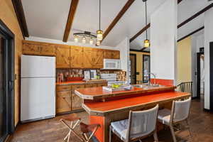 Kitchen with white appliances, dark hardwood / wood-style floors, and hanging light fixtures