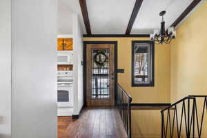 Entrance foyer featuring beamed ceiling, dark wood-type flooring, and an inviting chandelier