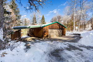 View of snowy exterior with a garage, a carport, and an outdoor structure