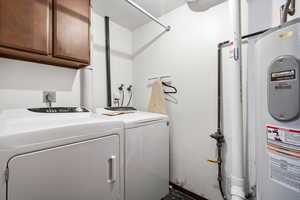 Clothes washing area with cabinets, electric water heater, and washing machine and clothes dryer