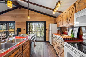 Kitchen featuring sink, lofted ceiling with beams, dark hardwood / wood-style floors, wood walls, and white appliances