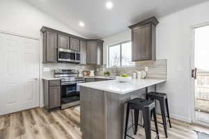 Kitchen with a kitchen bar, backsplash, stainless steel appliances, vaulted ceiling, and light hardwood / wood-style flooring