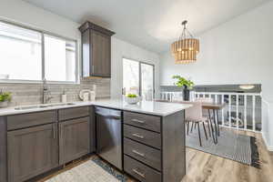 Kitchen featuring kitchen peninsula, sink, light hardwood / wood-style flooring, dishwasher, and hanging light fixtures