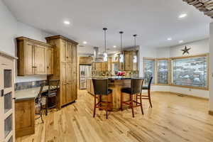 Kitchen with decorative backsplash, light wood-type flooring, island range hood, stainless steel fridge with ice dispenser, and hanging light fixtures