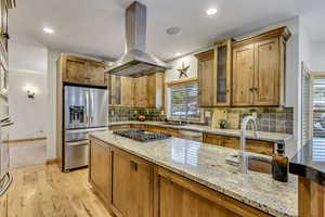 Kitchen featuring light stone countertops, island exhaust hood, appliances with stainless steel finishes, and tasteful backsplash