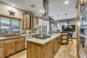 Kitchen featuring pendant lighting, a center island with sink, light wood-type flooring, appliances with stainless steel finishes, and island exhaust hood