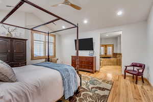 Bedroom with ensuite bath, ceiling fan, light hardwood / wood-style floors, and vaulted ceiling