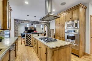 Kitchen with island exhaust hood, appliances with stainless steel finishes, light wood-type flooring, pendant lighting, and a center island