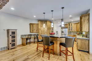 Kitchen featuring stainless steel fridge with ice dispenser, backsplash, island exhaust hood, pendant lighting, and light hardwood / wood-style floors