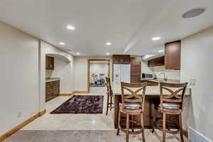 Kitchen featuring white refrigerator with ice dispenser, light tile patterned floors, a kitchen breakfast bar, and sink