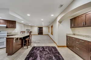 Kitchen with a kitchen breakfast bar, light stone counters, dark brown cabinets, white stove, and light tile patterned flooring