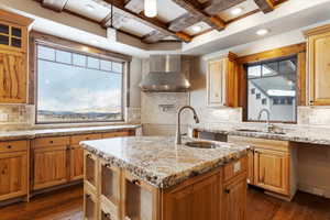 Kitchen with wall chimney exhaust hood, plenty of natural light, an island with sink, and coffered ceiling