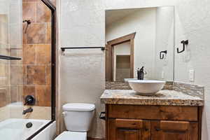 Full bathroom featuring tasteful backsplash, vanity, bath / shower combo with glass door, and toilet