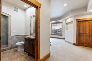 Bathroom featuring a tile shower, vanity, toilet, and tile walls