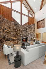 Carpeted living room with a stone fireplace, beamed ceiling, and high vaulted ceiling