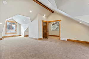 Additional living space featuring light carpet and lofted ceiling with beams