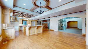 Kitchen featuring coffered ceiling, light hardwood / wood-style flooring, a spacious island, and decorative light fixtures