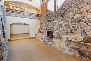 Living room with ceiling fan, carpet floors, a fireplace, and a high ceiling