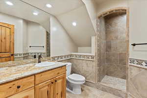 Bathroom with tiled shower, vanity, toilet, and tile walls