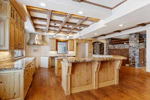 Kitchen with coffered ceiling, wall chimney exhaust hood, beam ceiling, light hardwood / wood-style floors, and a large island