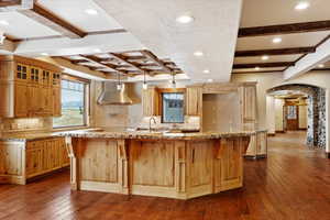 Kitchen featuring beamed ceiling, a large island with sink, dark hardwood / wood-style flooring, and ventilation hood