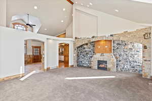 Unfurnished living room with carpet flooring, high vaulted ceiling, ceiling fan, and a stone fireplace