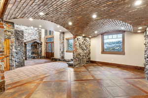 Unfurnished living room with a stone fireplace, a healthy amount of sunlight, and brick ceiling