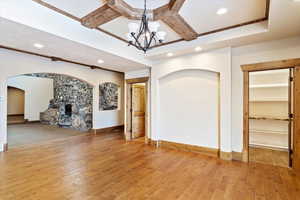 Unfurnished living room featuring a fireplace, beamed ceiling, wood-type flooring, and a notable chandelier