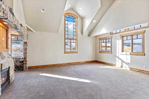 Unfurnished living room featuring carpet flooring, a fireplace, and high vaulted ceiling