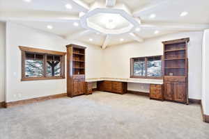 Unfurnished office featuring beam ceiling, light carpet, and built in desk