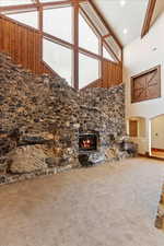 Unfurnished living room with carpet flooring, a stone fireplace, high vaulted ceiling, and beam ceiling