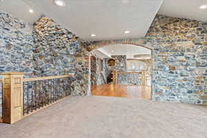 Unfurnished living room with carpet, lofted ceiling, and a textured ceiling