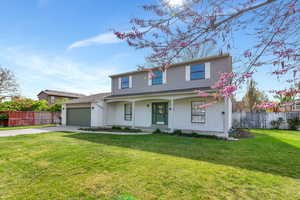 Traditional-style home featuring an attached garage, driveway, a front lawn, and fence