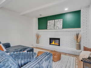 Living room featuring beam ceiling, a brick fireplace, and light wood-type flooring