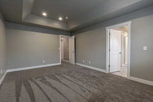 Unfurnished bedroom featuring a tray ceiling and light colored carpet