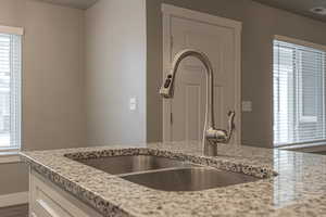 Kitchen with white cabinets, light stone counters, and sink