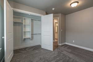 Unfurnished bedroom with a textured ceiling, dark carpet, and a closet