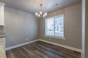 Unfurnished dining area with a textured ceiling, an inviting chandelier, and dark wood-type flooring