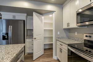 Kitchen with light stone countertops, light hardwood / wood-style flooring, white cabinets, and appliances with stainless steel finishes