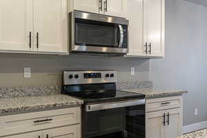 Kitchen with light stone counters, white cabinetry, and stainless steel appliances